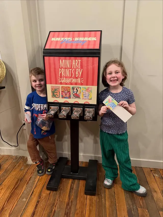 Two children beside the machine, holding their prints